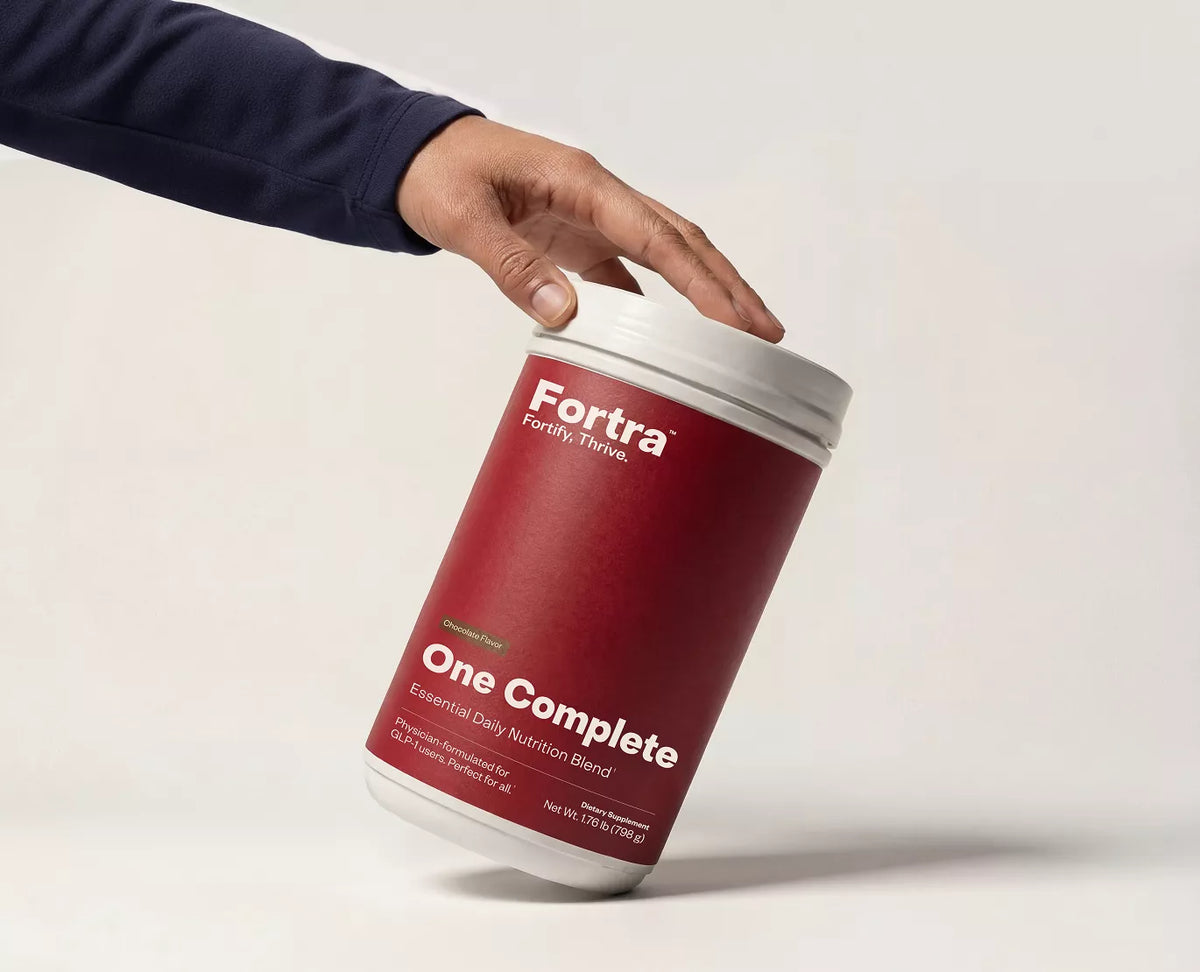 Person holding a red container labeled 'Fortra One Complete' on a light gray background