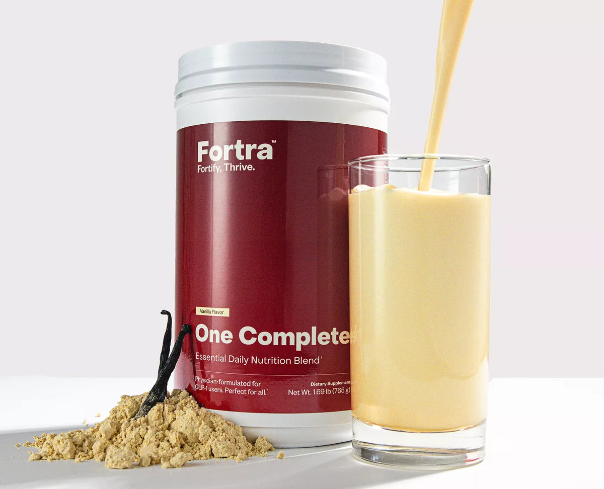 Fortra One Complete supplement container with a glass of vanilla shake and vanilla powder on a white background