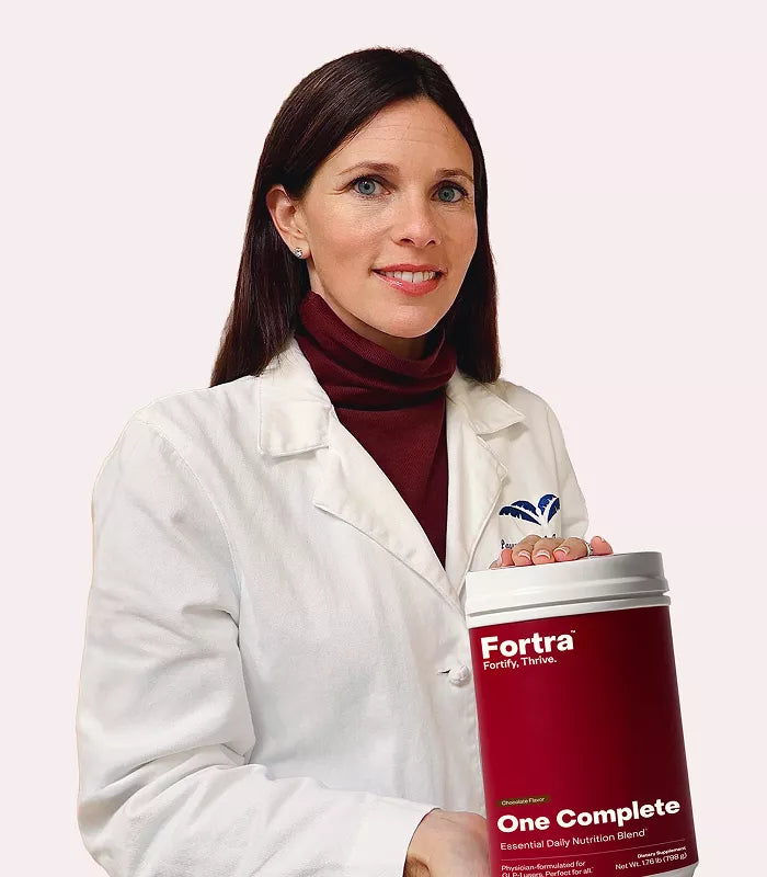 Woman in a white coat holding a large container labeled 'Fortra One Complete' against a light pink background